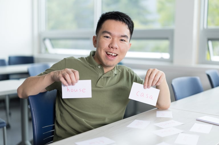 Young man holding English and Spanish flashcards in a classroom. Smiling while studying new vocabulary words.