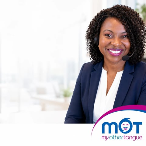 Professional woman with curly dark hair wearing navy blazer and white blouse, smiling in modern office setting with MOT logo